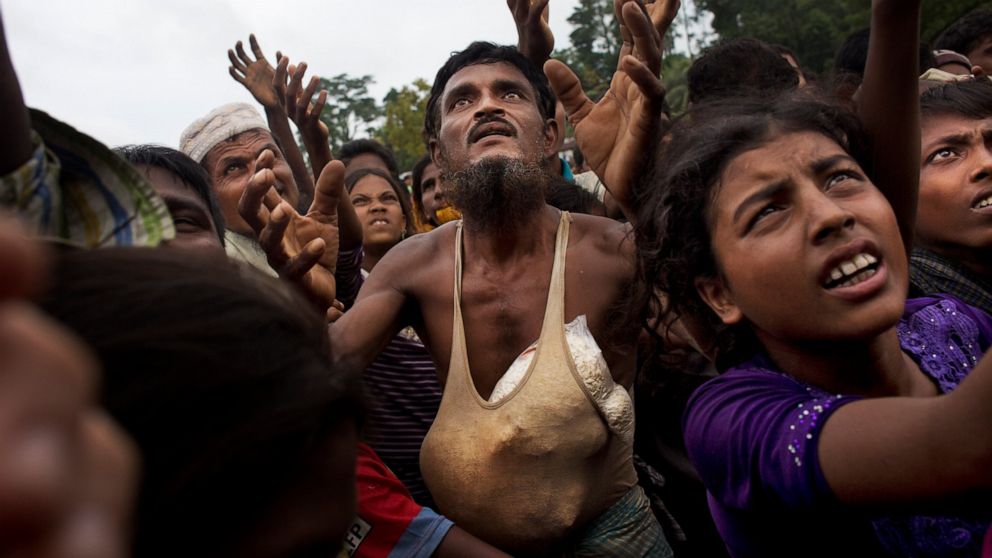 FILE- A Rohingya man stretches his arms out for food distributed by local volunteers, with bags of puffed rice stuffed into his vest at Kutupalong, Bangladesh, Sept. 9, 2017. Bangladesh’s prime minister said Monday that the prolonged stay of more tha